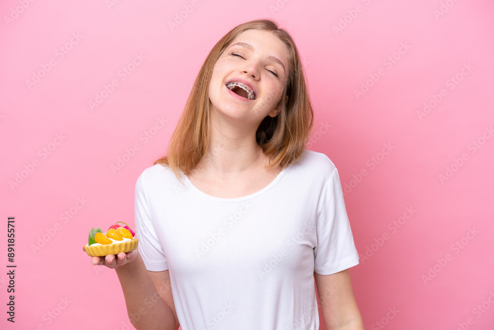 Teenager Russian girl holding a tartlet isolated on pink background laughing Teenager Russian girl holding a tartlet isolated on pink background laughing