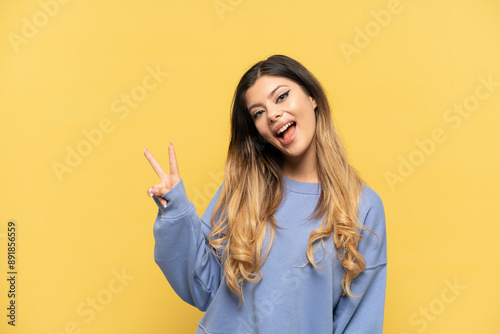 Young Russian girl isolated on yellow background smiling and showing victory sign