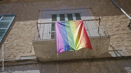 Rainbow flag hanging from a balcony on a sunny stone building representing lgbtq pride and inclusivity outdoors.