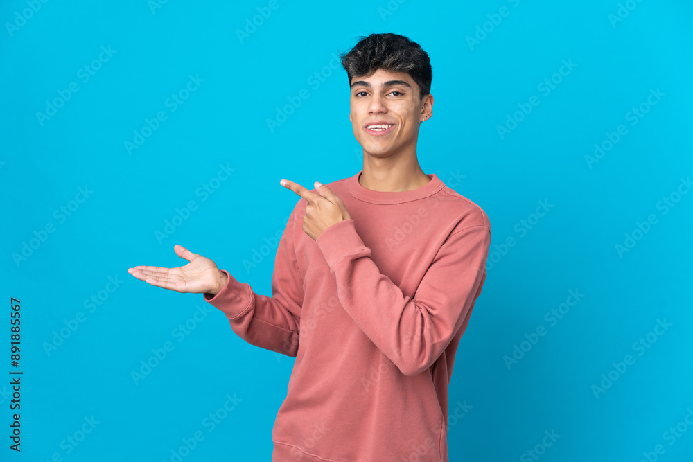 Young man over isolated blue background holding copyspace imaginary on the palm to insert an ad Young man over isolated blue background holding copyspace imaginary on the palm to insert an ad