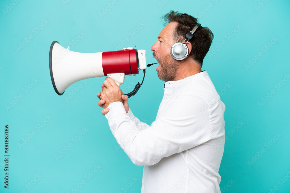 Telemarketer caucasian man working with a headset isolated on blue background shouting through a megaphone Telemarketer caucasian man working with a headset isolated on blue background shouting through a megaphone