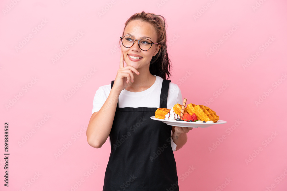 Restaurant waiter Russian girl holding waffles isolated on pink background thinking an idea while looking up Restaurant waiter Russian girl holding waffles isolated on pink background thinking an idea while looking up