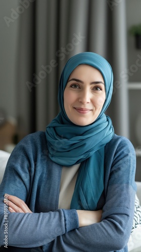 A woman wearing a blue hijab sits with her arms crossed