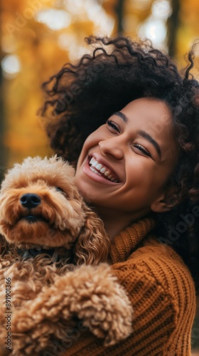A Black woman with curly hair smiles brightly while holding a small dog