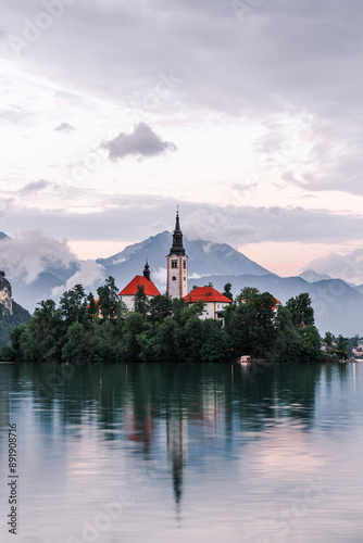 Bled, Slovenia (Slovenija), A chatolic church on the island in the lake by the mountainside with the castle on the big cliffed rock behind it in the evening hours with small partial clouds over them. photo