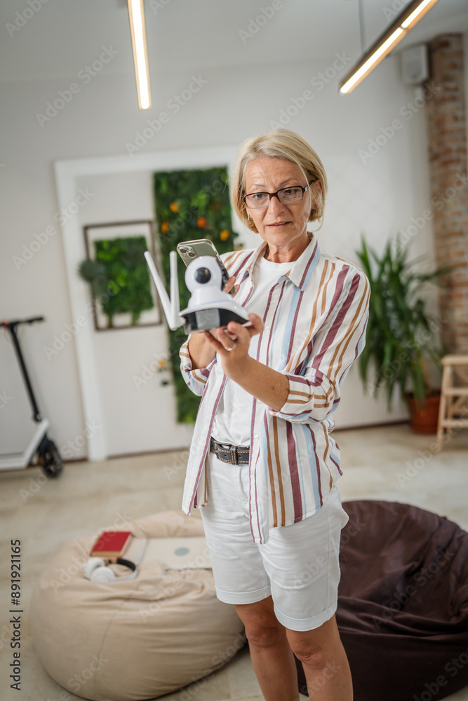 © Miljan Živković - woman mature caucasian hold adjust home security camera and smartphone