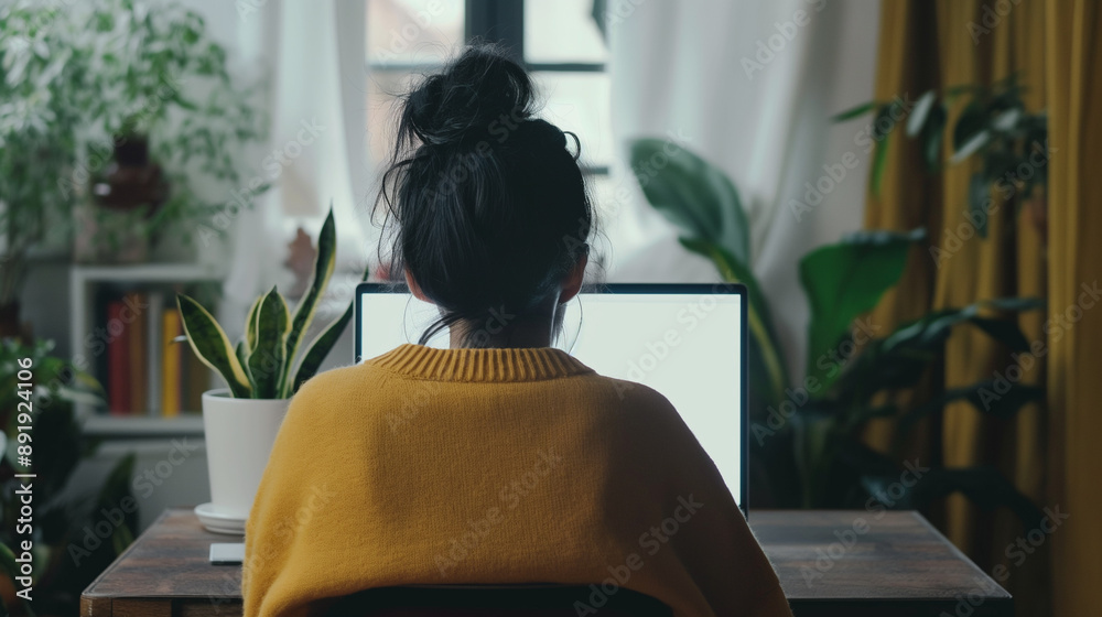 Over shoulder shot of a young Woman using computer laptop in front of an blank white computer screen in home