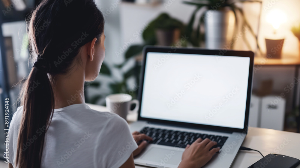 Over shoulder shot of a young Woman using computer laptop in front of an blank white computer screen in home Over shoulder shot of a young Woman using computer laptop in front of an blank white computer screen in home