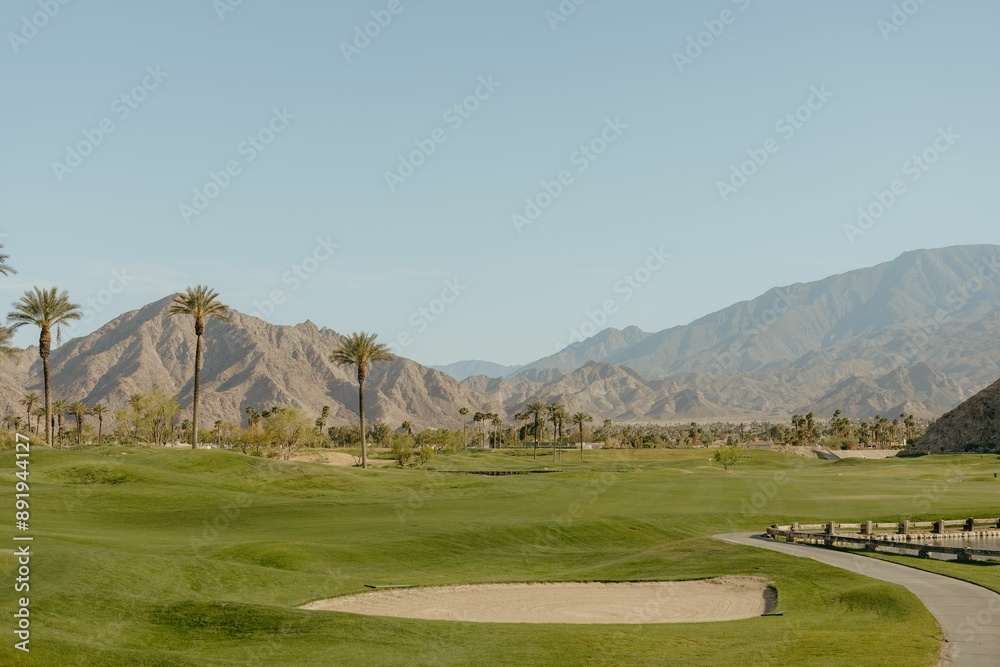 Fototapeta premium Scenic view of a golf course with mountains and palm trees under a clear blue sky