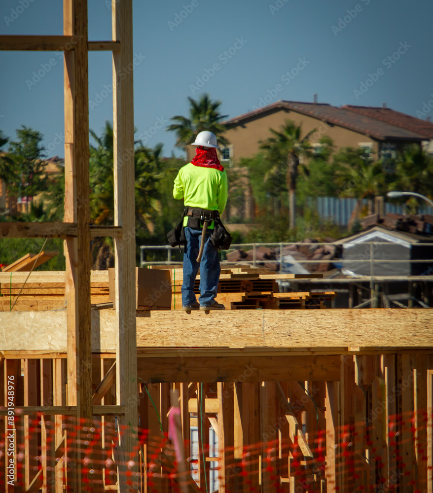 Direct view of a construction worker in green shirt standing on the top of a wood framing with a mountain in the background Direct view of a construction worker in green shirt standing on the top of a wood framing with a mountain in the background