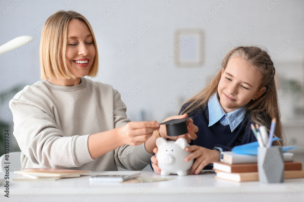 Mother with her daughter putting mortar board on piggy bank at home. Education savings concept Mother with her daughter putting mortar board on piggy bank at home. Education savings concept