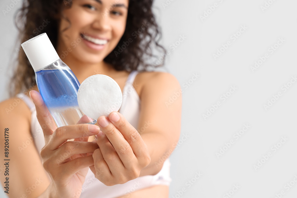Young African-American woman with micellar water and cotton pad on light background, closeup Young African-American woman with micellar water and cotton pad on light background, closeup