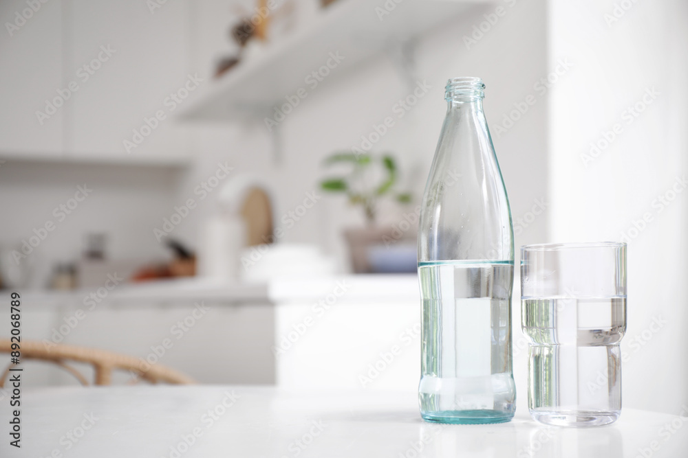 Bottle of water with glass on table in kitchen, closeup