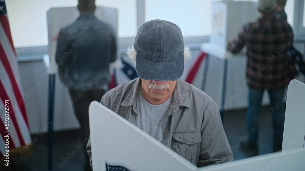 Elderly man stands at voting booth in polling station office. National Election Day in the United States. Political races of US presidential candidates. Patriotism and civic duty concept. Dolly shot. Elderly man stands at voting booth in polling station office. National Election Day in the United States. Political races of US presidential candidates. Patriotism and civic duty concept. Dolly shot.