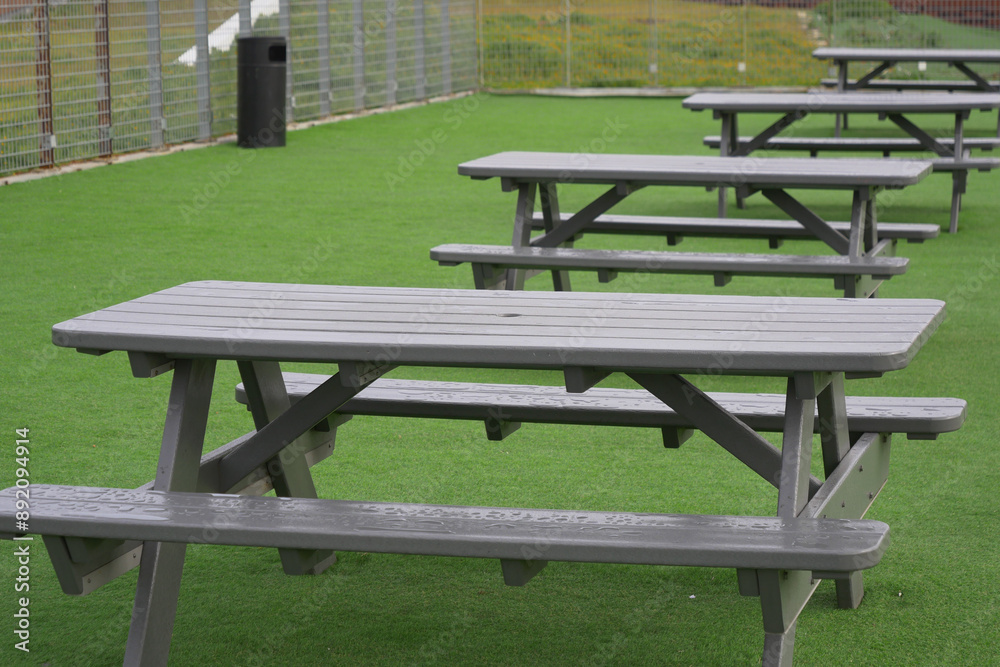 The parks artificial grass area features empty picnic tables under the sunny sky The parks artificial grass area features empty picnic tables under the sunny sky