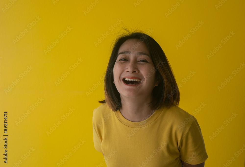 Asian woman standing shocked laughing isolated over yellow background surprised and wearing round neck shirt orange,looking at the camara and happy Asian woman standing shocked laughing isolated over yellow background surprised and wearing round neck shirt orange,looking at the camara and happy