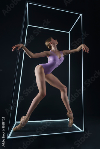 ballerina in a photo studio on a black background in a light led cube shows ballet elements and stretching photo