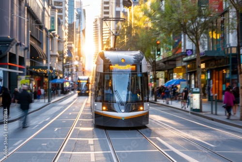 A modern tram travels down a bustling city street with the sun setting in the background. photo