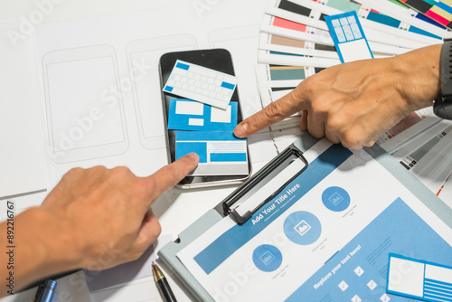 A group of people collaborates around a desk, discussing and reviewing user interface (UI) and user experience (UX) elements. usability, accessibility, and design principles for product development. photo