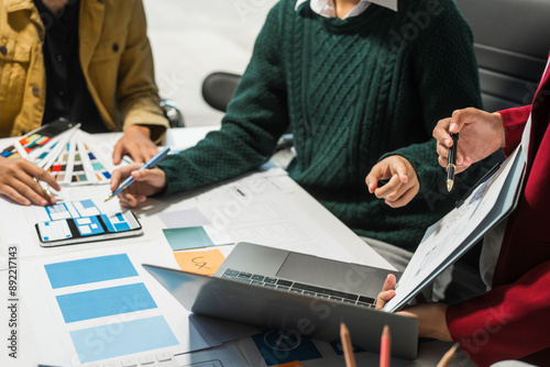 A group of people collaborates around a desk, discussing and reviewing user interface (UI) and user experience (UX) elements. usability, accessibility, and design principles for product development.