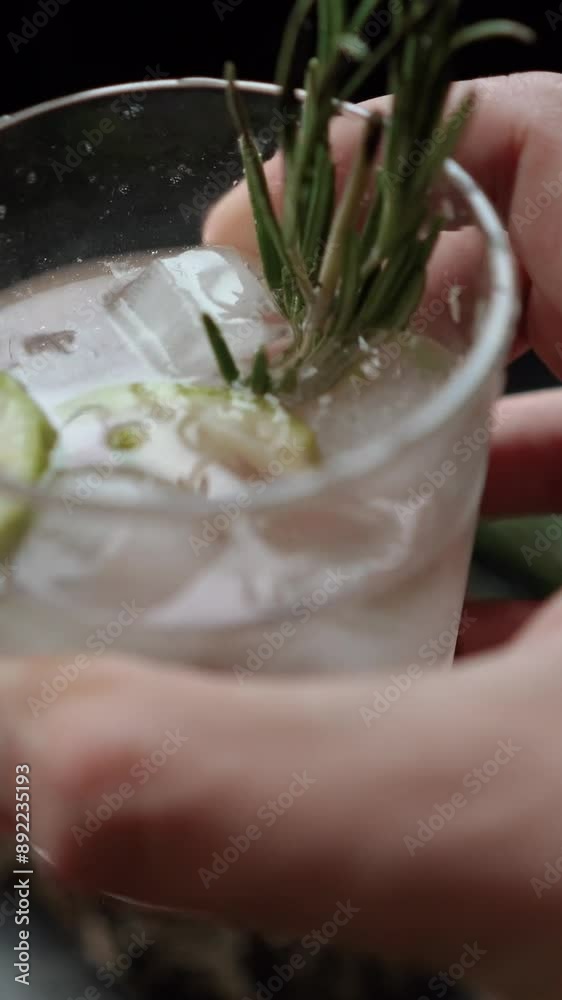 Ice cubes fall into a glass with lime and rosemary and topped with soda. The process of preparing a cocktail and a refreshing summer drink with alcohol for a party. Cold water with gin Ice cubes fall into a glass with lime and rosemary and topped with soda. The process of preparing a cocktail and a refreshing summer drink with alcohol for a party. Cold water with gin