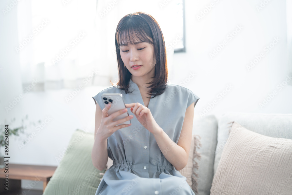 ソファに座り携帯を見て悩む女性 ソファに座り携帯を見て悩む女性