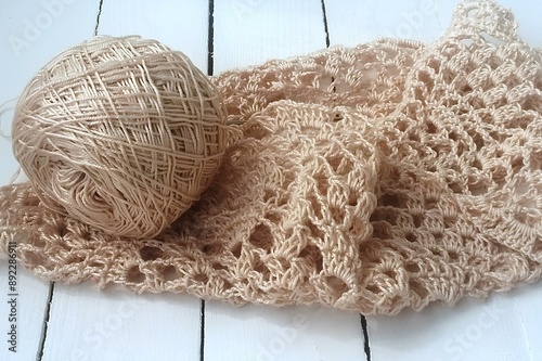 a ball of beige yarn next to a piece of crocheted fabric. The fabric has an open, lacy pattern and is made from the same yarn as the ball. The background is a white wooden surface photo