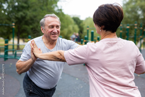 Elderly man and woman doing gymnastics on an outdoor sports ground photo