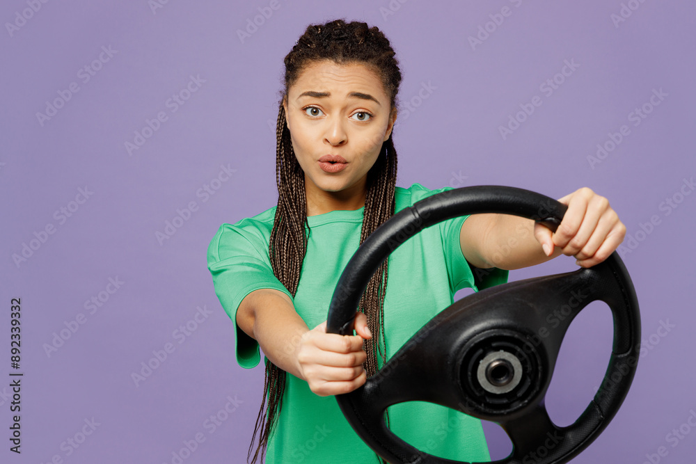 Young scared woman of African American ethnicity with dreadlocks wear green t-shirt casual clothes hold steering wheel driving car isolated on plain pastel light purple background. Lifestyle concept. Young scared woman of African American ethnicity with dreadlocks wear green t-shirt casual clothes hold steering wheel driving car isolated on plain pastel light purple background. Lifestyle concept.