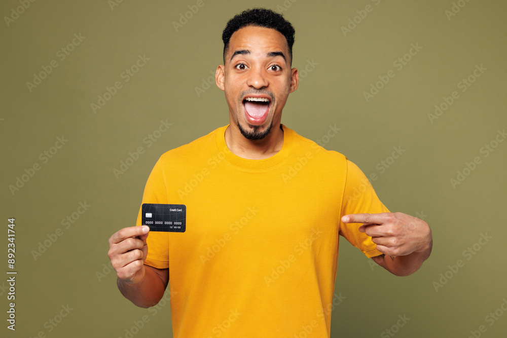 Young man of African American ethnicity he wearing yellow t-shirt casual clothes hold in hand point on mock up of credit bank card isolated on plain pastel green background studio. Lifestyle concept. Young man of African American ethnicity he wearing yellow t-shirt casual clothes hold in hand point on mock up of credit bank card isolated on plain pastel green background studio. Lifestyle concept.