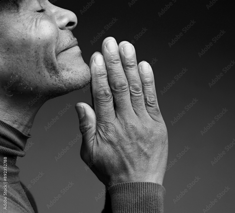 Fototapeta premium man praying to god with hands together Caribbean man praying with black background with people stock photo