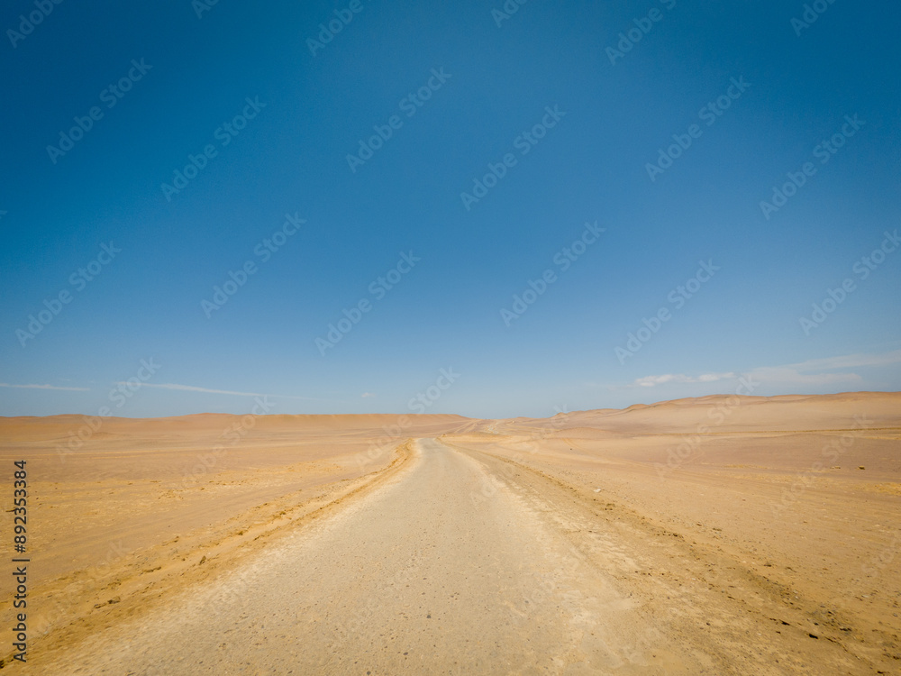 Desert road curving through sandy landscape under clear blue sky. Outdoor travel and adventure concept. Aerial view of desert route. Desert road curving through sandy landscape under clear blue sky. Outdoor travel and adventure concept. Aerial view of desert route.