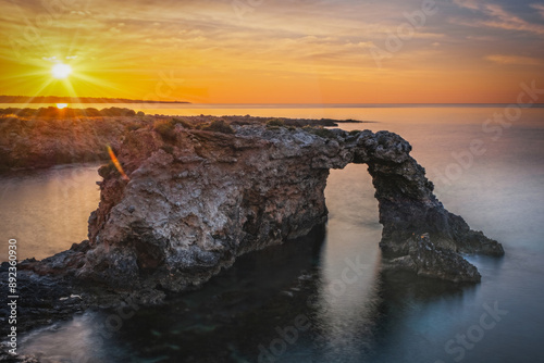 Rocky coastline with a natural arch at punta Asparano, near Siracusa. Sunrise time, long exposure picture. June 2023