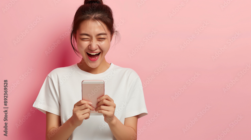 Young Asian woman in white t-shirt, excitedly celebrating with a smartphone against a pink background. Young Asian woman in white t-shirt, excitedly celebrating with a smartphone against a pink background.