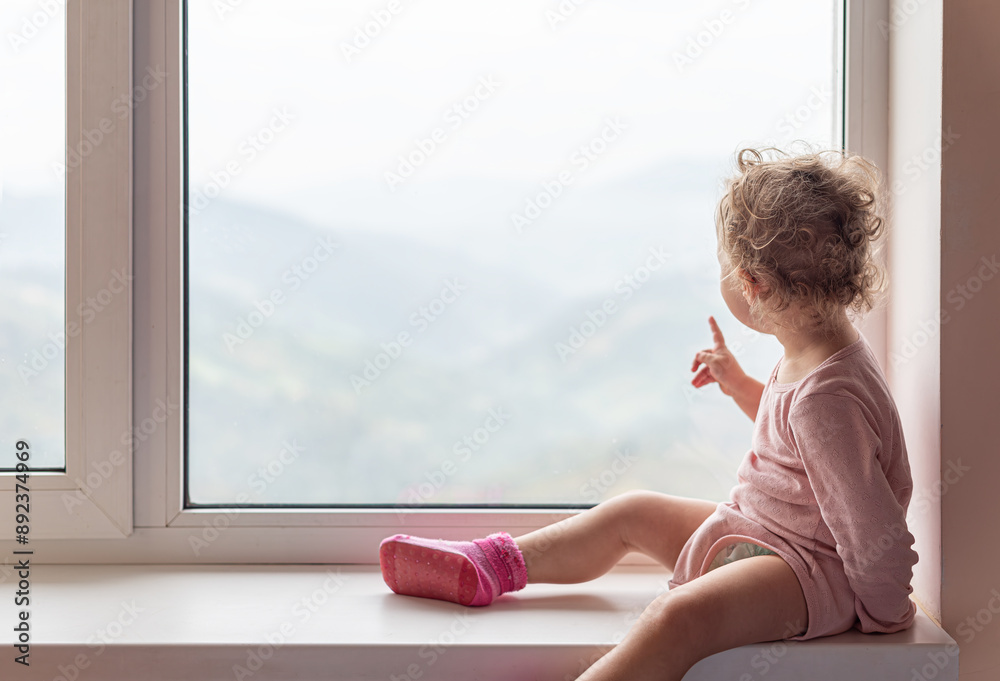 A small child in pajamas sits on the windowsill.