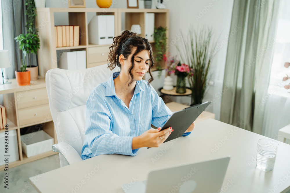 One young beautiful caucasian business woman working in office on laptop and looking through charts One young beautiful caucasian business woman working in office on laptop and looking through charts