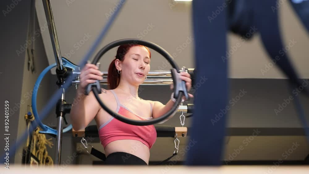A young red-haired woman reshaping her body through exercises on a Reformer Pilates machine in a Pilates studio A young red-haired woman reshaping her body through exercises on a Reformer Pilates machine in a Pilates studio