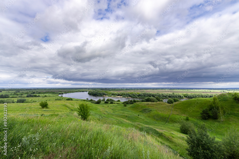 A picturesque scene of rolling green hills with a winding river in the distance. The sky is overcast with dramatic clouds, suggesting an approaching storm. A picturesque scene of rolling green hills with a winding river in the distance. The sky is overcast with dramatic clouds, suggesting an approaching storm.