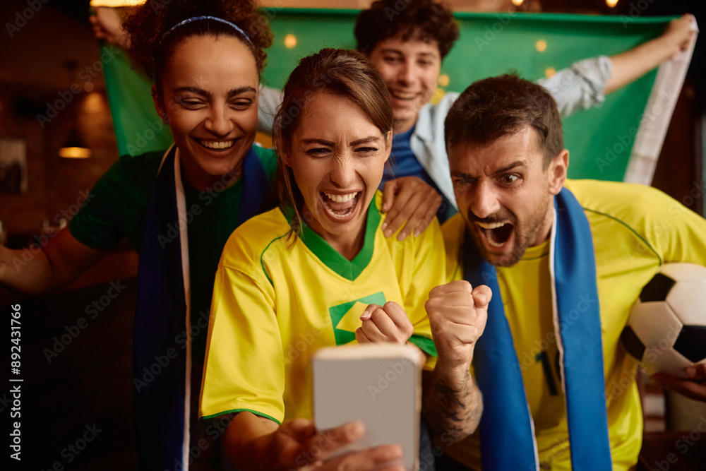 Fototapeta premium Excited soccer fans cheering while watching match on smart phone.