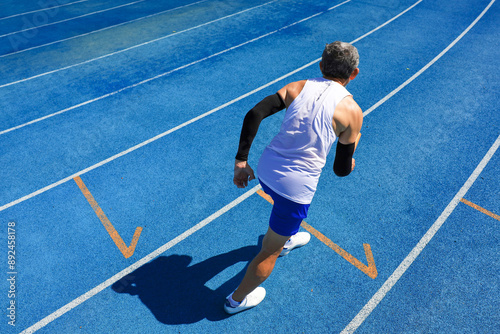 Senior Asian athlete is practicing running with relay baton in the professional blue track for professional exercise, sport training workout and healthy for longevity