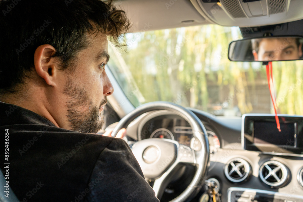 Hombre elegante sentado en su auto nuevo mirando a cámara desde el espejo retrovisor Hombre elegante sentado en su auto nuevo mirando a cámara desde el espejo retrovisor
