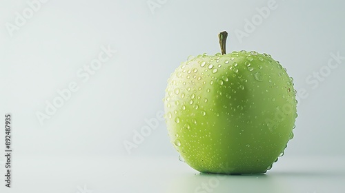 A green apple with water drops on its skin. The apple is sitting on a white surface. The background is white. photo