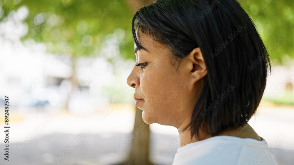 Mature hispanic woman in profile, outdoors with blurred green park background, embodying urban tranquility. Mature hispanic woman in profile, outdoors with blurred green park background, embodying urban tranquility.