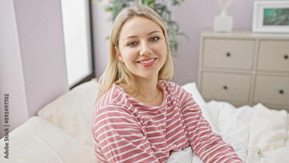 A young, attractive, blonde woman smiles gently while sitting comfortably in a bright, cozy bedroom A young, attractive, blonde woman smiles gently while sitting comfortably in a bright, cozy bedroom