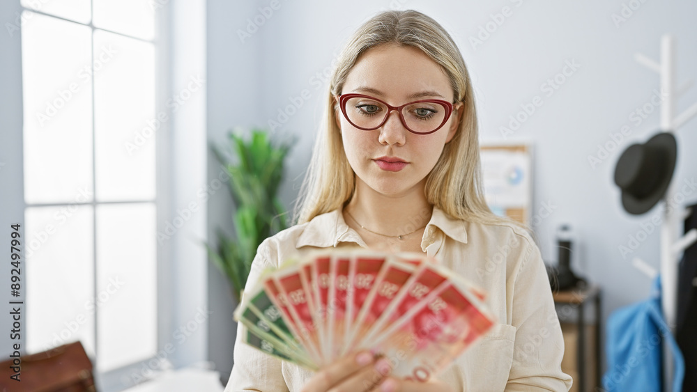 Young caucasian woman in office holding israeli shekels, looking serious and professional.