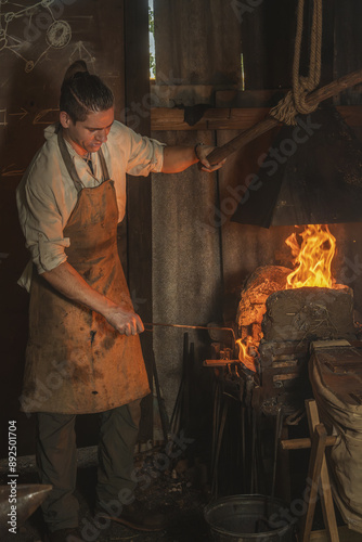 Blacksmith heats a metal part in a fire before forging it in an old village forge. Traditional crafts