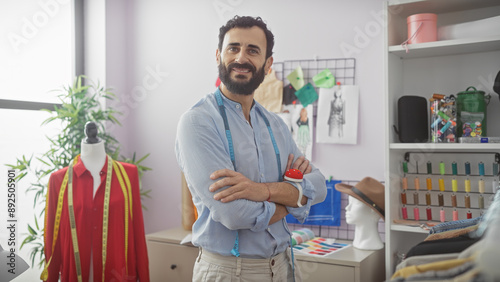 Confident male tailor with beard standing arms crossed in a design room surrounded by mannequins, fabric, and threads. photo