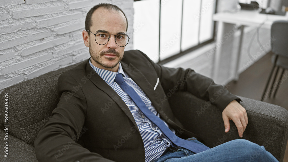 Confident businessman sitting in a modern office, wearing glasses and a suit, portrays professionalism. Confident businessman sitting in a modern office, wearing glasses and a suit, portrays professionalism.