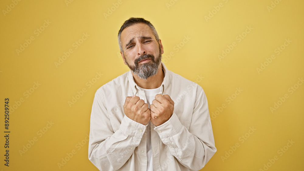 A distressed senior hispanic man with a beard and grey hair against a yellow isolated background A distressed senior hispanic man with a beard and grey hair against a yellow isolated background
