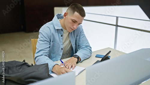 A focused young man studying at an indoor university setting, conveying a sense of dedication and academic pursuit.